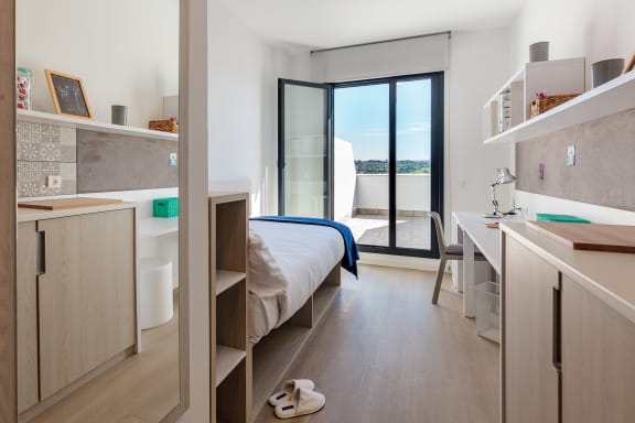 a bedroom with a bed and a desk and a balcony
