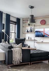 A living room with a black couch and a grey blanket.