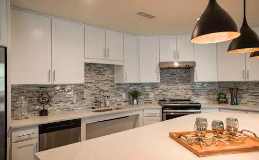 A kitchen with white cabinets and a marble backsplash.