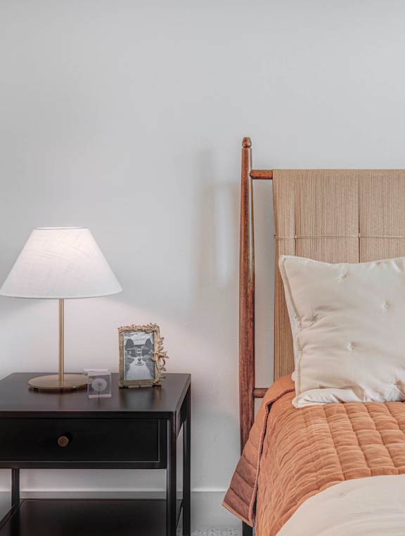 A bed with a white pillow and a grey pillow is next to a lamp on a small table.