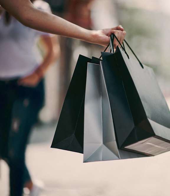 A person is holding three black shopping bags.