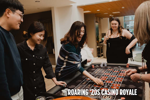 A group of people playing a game on a table with the words "ROARING '20s CASINO ROYALE" on it.