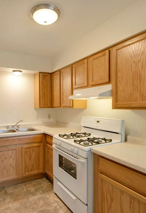 A kitchen with a white stove and wooden cabinets. at Northeast Villas, Fridley, 55421