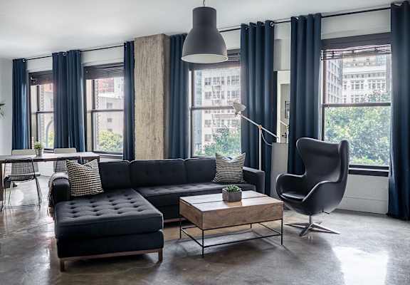 A black couch with a wooden coffee table in front of a window with a chair and a floor lamp.