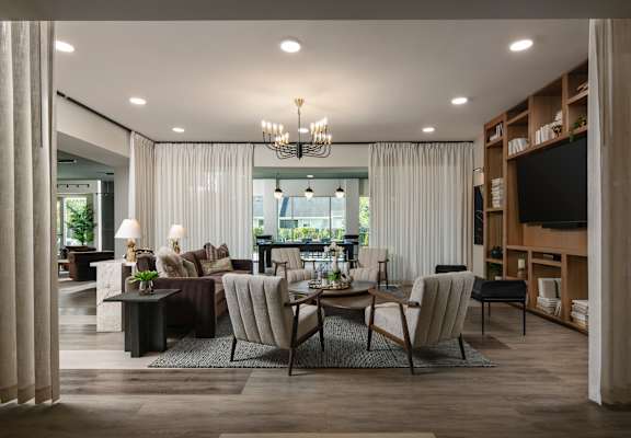 A modern living room with a large window, a sofa, a chair, a coffee table, and a chandelier.at Address East End, Raleigh