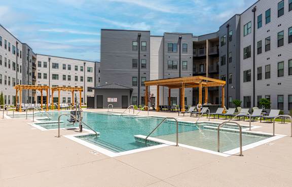 A swimming pool area with a wooden pavilion and lounge chairs.