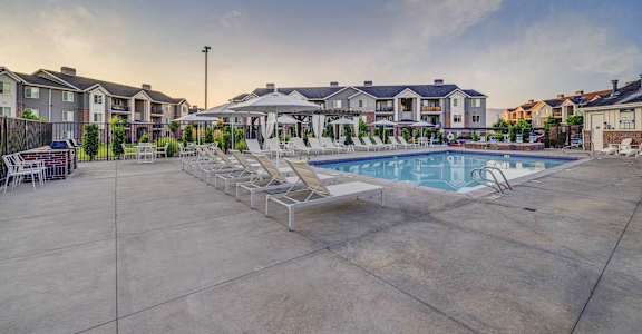 A large outdoor swimming pool surrounded by lounge chairs and buildings in the background.