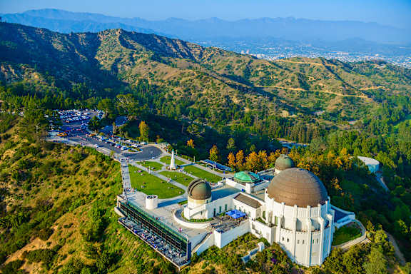 A large white building with a brown dome is surrounded by a green landscape.
