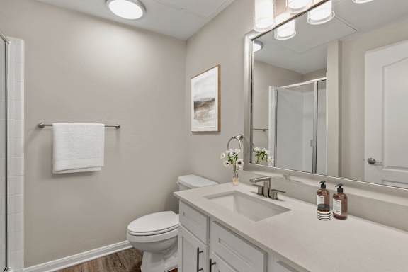 A bathroom with a toilet, sink, mirror, and a white towel hanging on the wall.
