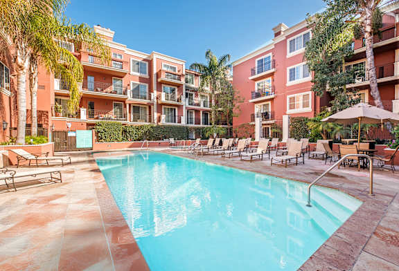 A swimming pool surrounded by lounge chairs and umbrellas in front of a red building.