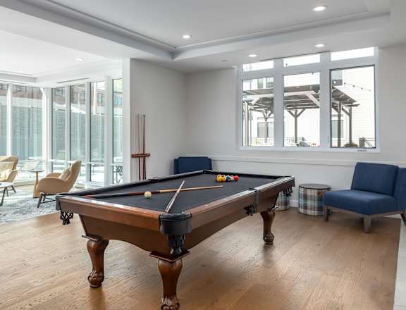 A pool table is in the middle of a room with a blue chair and a window. at 2200 LaSalle Apartments, Missouri, 63104