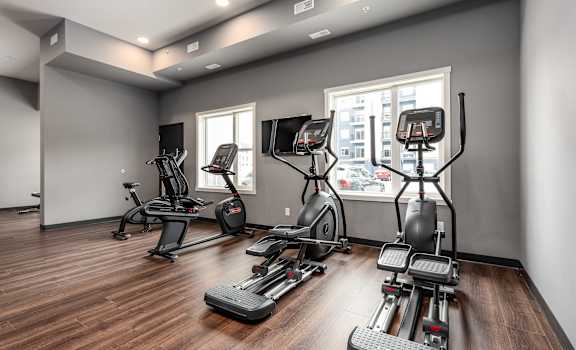 a gym with exercise equipment on a wooden floor and a window