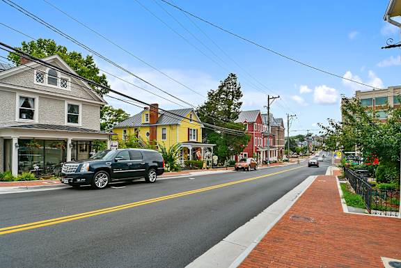A black SUV is driving down a street lined with colorful houses.