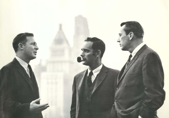 three men in suits standing in front of a city skyline