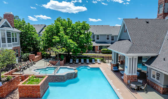 A large swimming pool surrounded by a brick wall and a patio area with chairs and a grill.