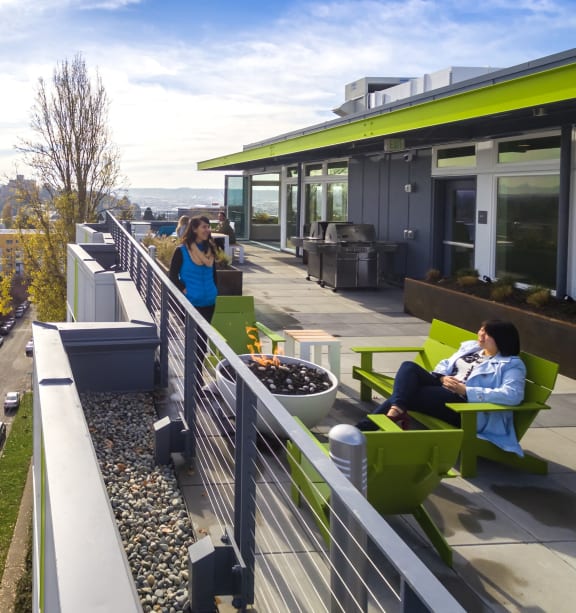 people sit on green chairs on a balcony with a view of the city in the background