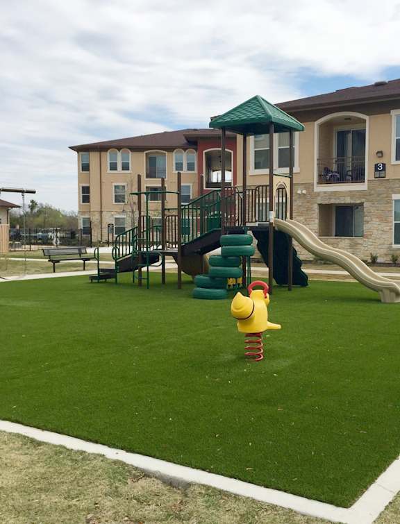 A playground with a yellow duck slide in front of a building.