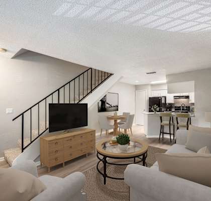 a living room with couches and a tv and a kitchen with a staircase