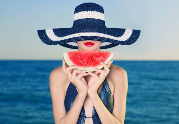 woman in hat eating watermelon on the beach