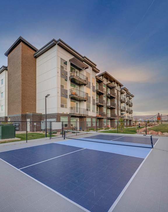 A tennis court is located in front of apartment buildings.