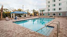 A swimming pool surrounded by a brick patio and a white building in the background.