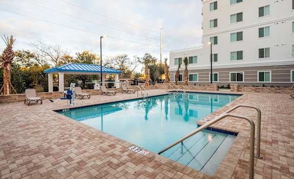 A swimming pool surrounded by a brick patio and a white building in the background.