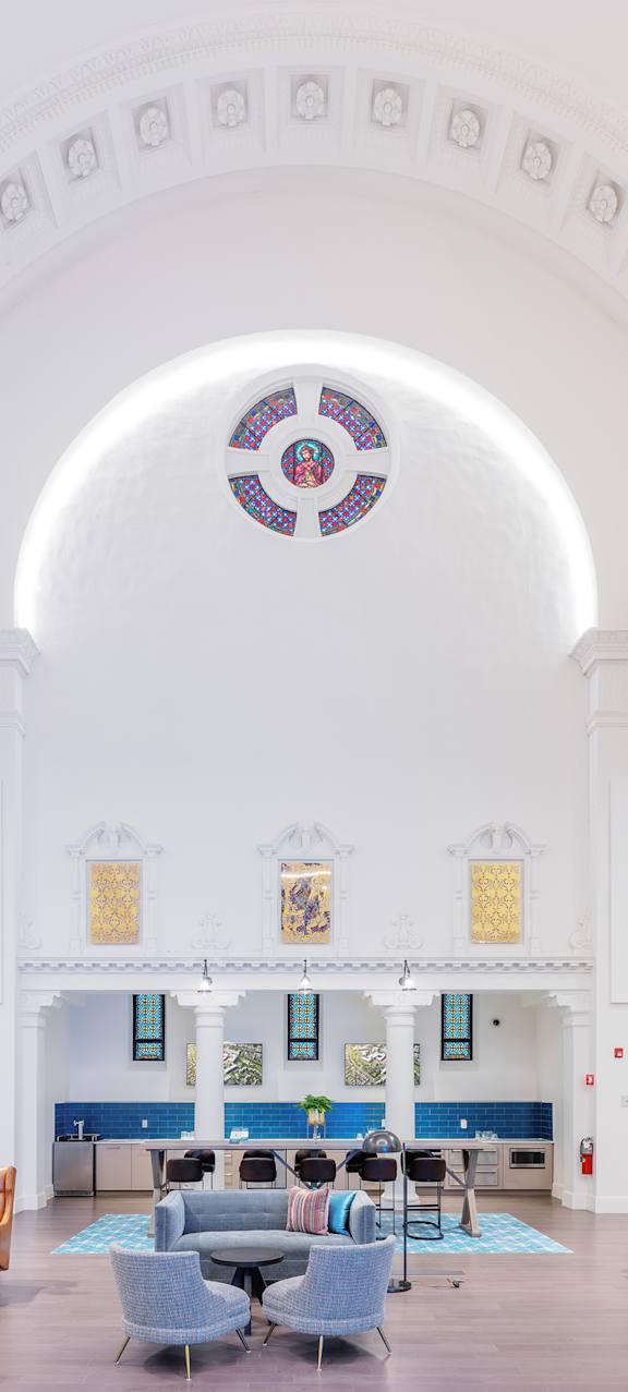 A white church interior with a stained glass window and a circular design on the ceiling.