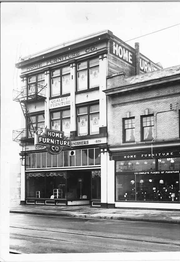 A black and white photo of a building with the words "Home Furniture" on it.