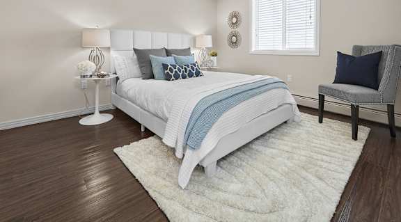 A bedroom with a white bed and a grey armchair.