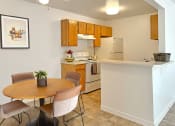 Thumbnail 5 of 17 - Bridgeside Landing Apartments in Taylorsville, Utah, Kitchen with wood cabinets, stove, fridge, dining area with round table and four chairs.