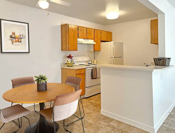 Bridgeside Landing Apartments in Taylorsville, Utah, Kitchen with wood cabinets, stove, fridge, dining area with round table and four chairs.