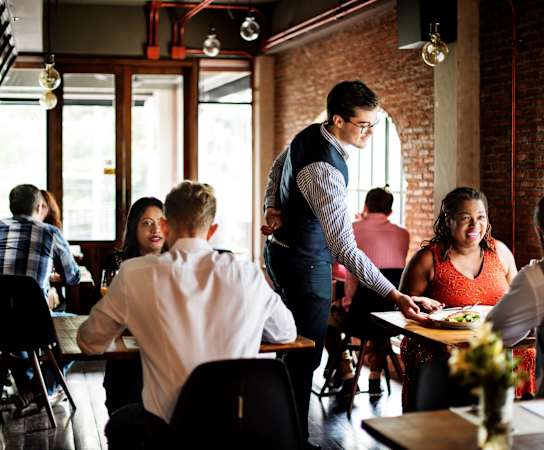 a waiter serves a plate of food to a group of people in a restaurant at Residences at Manchester Place, Manchester