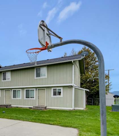 the basketball hoop is in the center of the concrete court in front of a house
