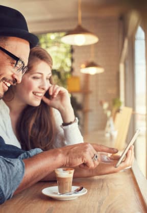 a man and woman sitting at a table in a coffee shop looking at a tablet