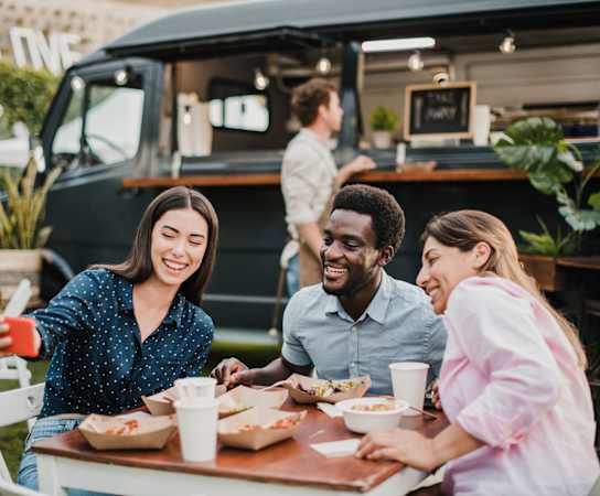 a group of people sitting at a table in front of a food truck at Saddleworth Green, Florida