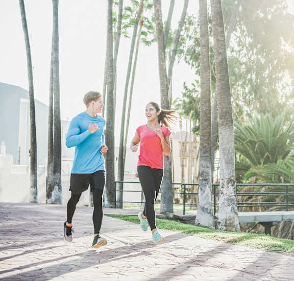 a man and a woman running on a sidewalk with palm trees in the background at Cypress Gardens, Cedar Park, 78613