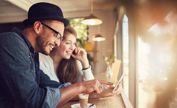 a man and woman sitting at a table in a coffee shop looking at a tablet  at Residences at Westborough Station, Westborough, 01581
