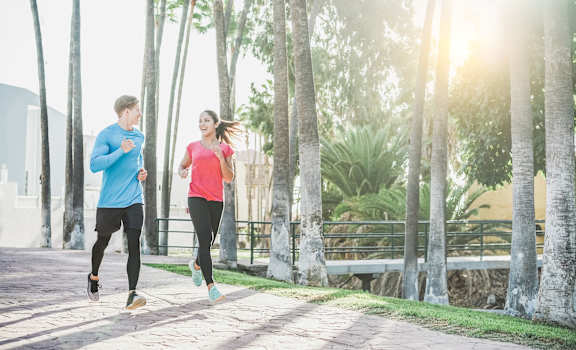 a man and a woman running on a sidewalk with palm trees in the background at Village at Terra Bella Apartments, Land O' Lakes, Florida