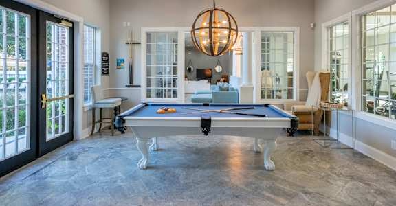 A pool table is in the middle of a room with a hanging light fixture.