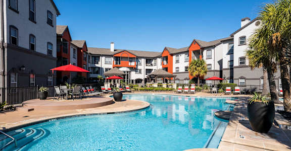 A swimming pool surrounded by a patio with chairs and umbrellas.