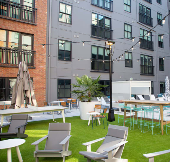 a grassy area with lounge chairs and tables and a pool in front of an apartment building