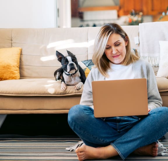 a woman sitting on the floor with her dog and laptop