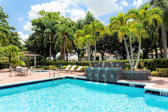 A pool surrounded by a brick patio and palm trees.