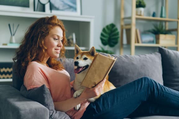 Woman sitting on couch with dog, reading