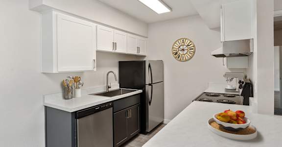 A kitchen with a black fridge and a clock on the wall.