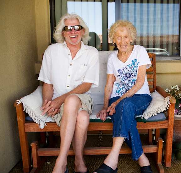 An elderly couple wearing sunglasses and sitting on a bench.