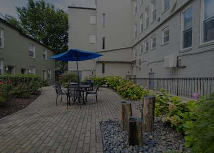 a patio with a table and umbrella in front of an apartment building at Queen Anne Belvedere, Maryland, 21201