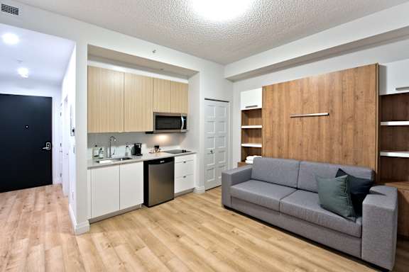 A modern kitchen with a grey couch and wooden cabinets.
