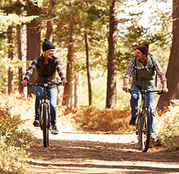 two men riding bikes on a trail through a forest