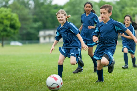 A group of children in blue uniforms playing soccer on a field.